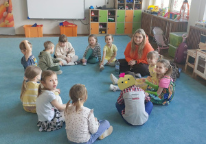 Dzieci i nauczycielka siedzą na dywanie i rozmawiają. Grupa 3