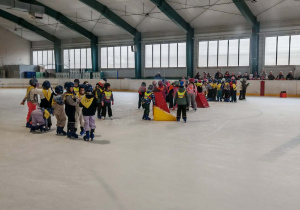 Drużyny zawodników ustawione w grupkach na tafli lodowiska.