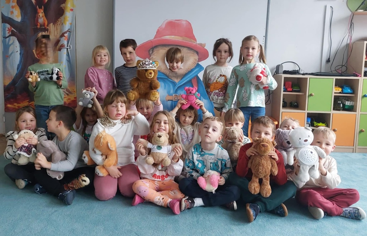 Dzieci pozują do wspólnego zdjęcia prezentując ulubione przytulanki - pluszowe misie.