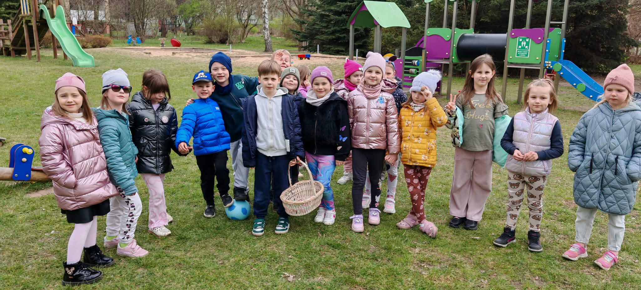 Dzieci z grupy 4 i 5 pozują do wsp&oacute;lnego zdjęcia w ogrodzie przedszkolnym. Dzieci trzymają koszyk.