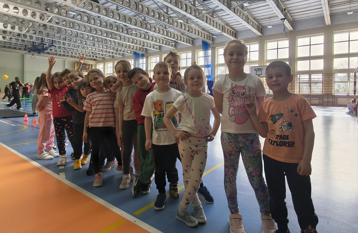 Grupa dzieci pozuje do wsp&oacute;lnego zdjęcia w dużej sali gimnastycznej SP44.