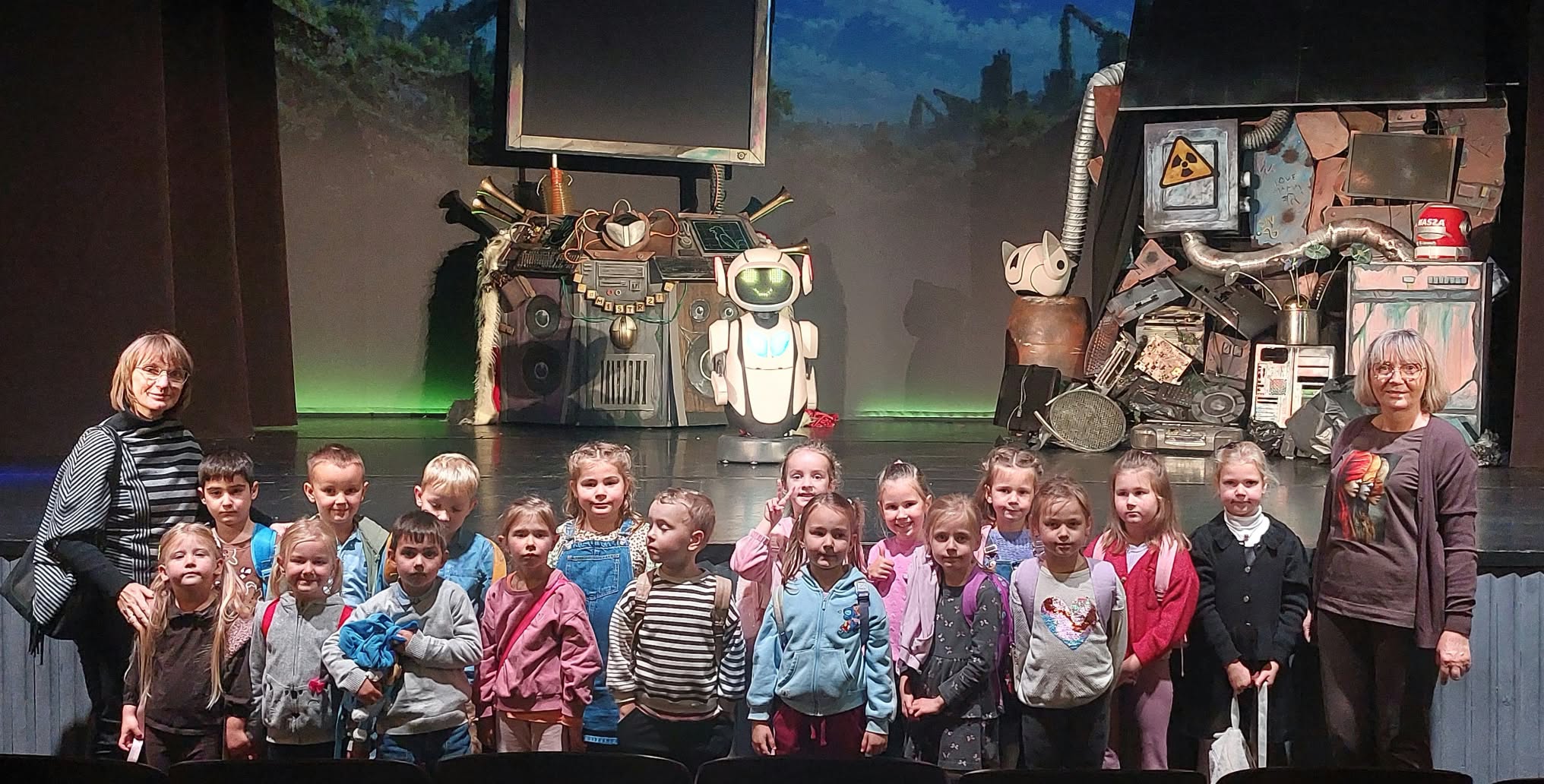 Grupa dzieci i nauczycielki pozują do wspólnego zdjęcia na tle sceny. Grupa 5.