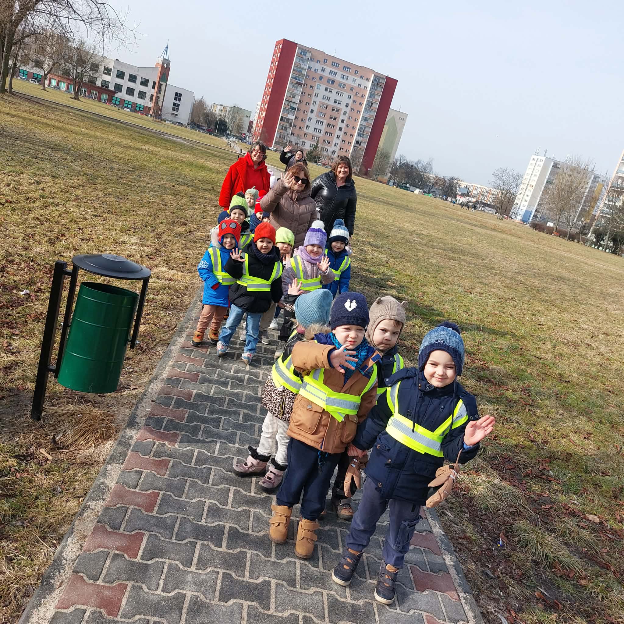 Duża grupa dzieci i nauczycielki pozują do wsp&oacute;lnego zdjęcia na tle blok&oacute;w Retkini. Ujęcie 1