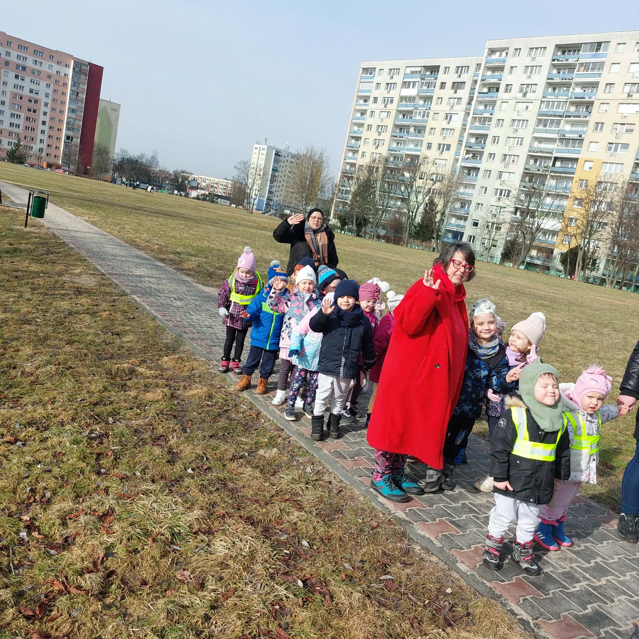 Duża grupa dzieci i nauczycielki pozują do wsp&oacute;lnego zdjęcia na tle blok&oacute;w Retkini. Ujęcie 2