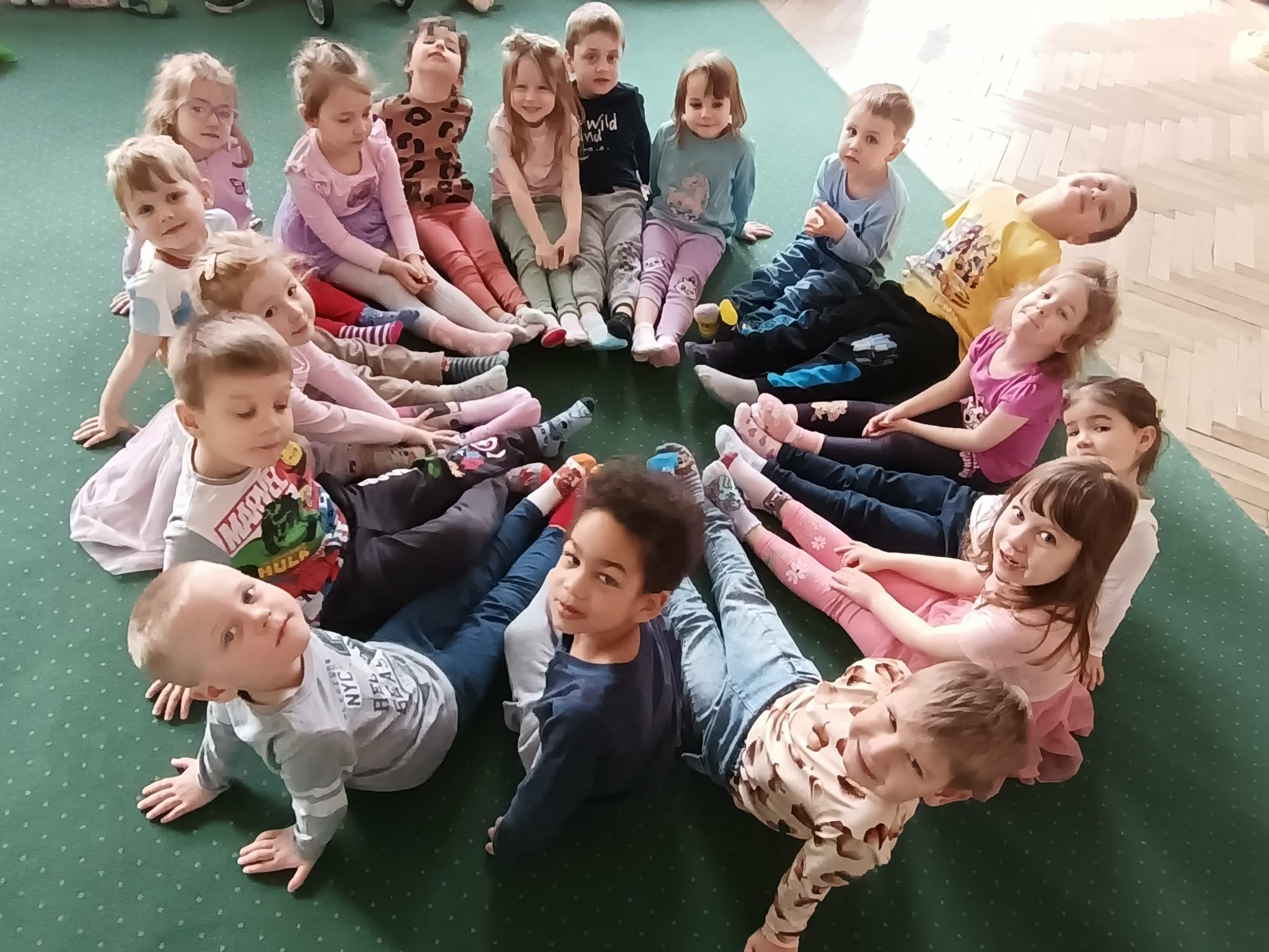 Dzieci z grupy 2 siedzą w ciasnym k&oacute;łeczku na dywanie prezentując kolorowe skarpetki.