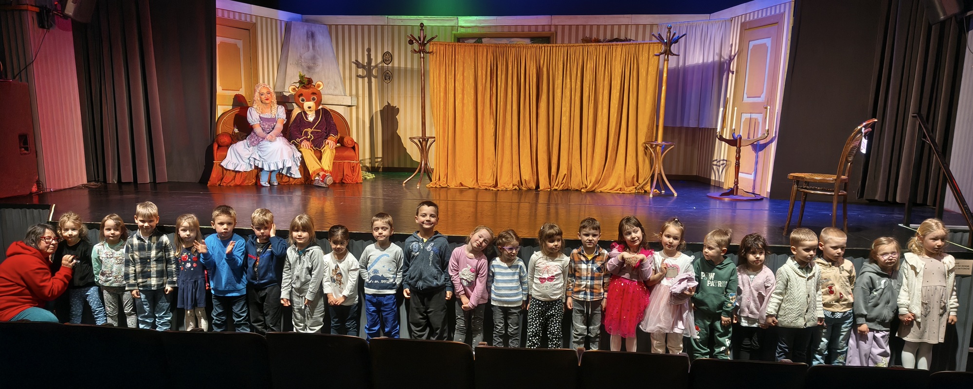 Dzieci pozują do wsp&oacute;lnego zdjęcia na tle sceny i aktor&oacute;w.