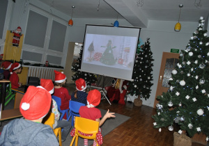 Dzieci oglądają na dużym ekranie nagranie występu "Pani Choinki". Dzieci mają na głowach czapki Mikołaja. Ujęcie 2