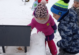 Dzieci wysypują karmę dla ptaków do karmnika. Dookoła jest dużo śniegu, a dzieci są ciepło ubrane. Ujęcie 1