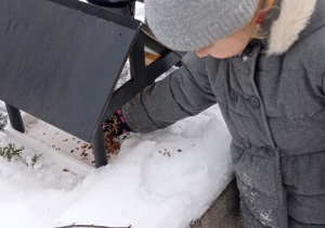Dzieci wysypują karmę dla ptaków do karmnika. Dookoła jest dużo śniegu, a dzieci są ciepło ubrane. Ujęcie 2