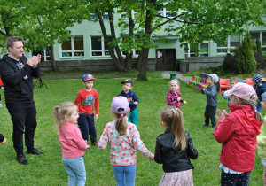 Dzieci tańczą w ogrodzie. Obok razem z dziećmi tańczy nauczyciel.