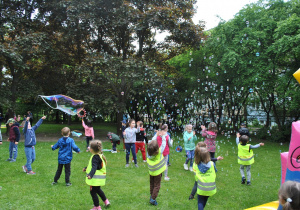 Duża grupa dzieci bawi się pomiędzy latającymi nad nimi mydlanymi bańkami.