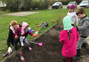 Rodzic i grupka dzieci porządkują grządkę w ogródku.