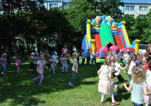 Dzieci biegną do konferansjerki. W tle dmuchany zamek. Ujęcie z lewej strony.