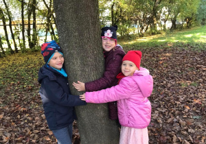 Troje dzieci przytula sie do drzewa.