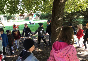 Dzieci trzymają się za ręce i tańczą dookoła drzewa. Ujęcie 2
