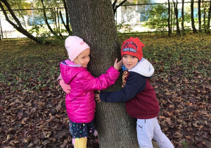 Dwoje dzieci przytula się do drzewa.