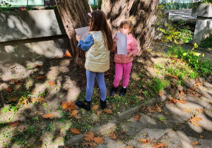Dwoje dzieci stoi obok drzewa.