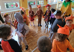 Dzieci tańczą z nauczycielką trzymając się za ręce.