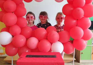 Dzieci pozują do pamiątkowego zdjęcia w fotobudce z czerwonych baloników.