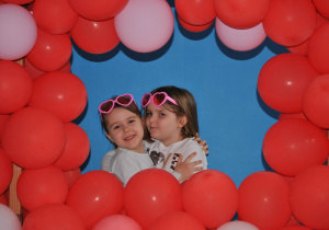 Dzieci pozują do pamiątkowego zdjęcia w fotobudce z czerwonych baloników.