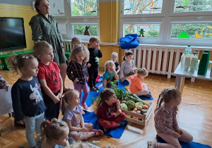Dzieci na widowni. Pomiędzy dziećmi stoi skrzynka z warzywami.