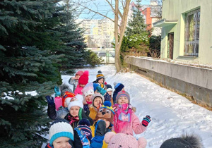 Grupa dzieci na zimowym spacerze. Obok budynek przedszkola.