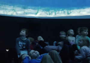 Dzieci wewnątrz namiotu oglądają film.