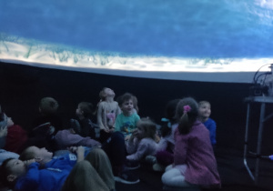 Dzieci wewnątrz namiotu oglądają film.