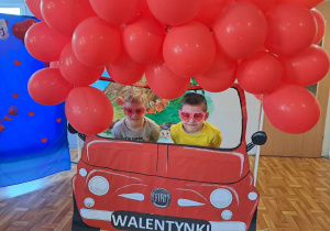 Dzieci pozują do wspólnego zdjęcia w fotobudce ozdobionej balonikami.