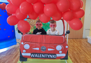 Dzieci pozują do wspólnego zdjęcia w fotobudce ozdobionej balonikami.