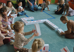 Dzieci siedzą na dywanie i układają duże domino obrazkowe z symbolami Polski.