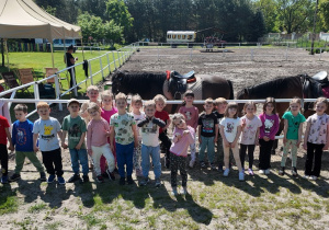 Dzieci pozują do pamiątkowego wspólnego zdjęcia w czasie wycieczki do Nieborowa. Grupa dzieci stoi przed padokiem z końmi.
