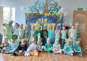 dzieci pozuje do wspólnego zdjęcia na tle napisu "Mam talent". Stroje dzieci są w różnych odcieniach zieleni.