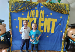 Dwoje dzieci pozuje do zdjęcia na tle ścianki z napisem "Mam talent".