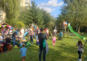 Dzieci i rodzice w czasie pobytu na pikniku wspólnie spędzają czas w części gastronomicznej i na zabawkach ogrodowych.
