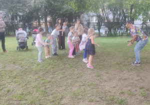 Dzieci tańczą razem z animatorem. Obok stoją rodzice i nauczycielka.