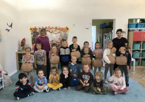 Dzieci i nauczycielka pozują do wspólnego zdjęcia w sali przedszkolnej. Dzieci trzymają fantomy do ćwiczeń RKO. Zdjęcie częściowo anonimizowane.