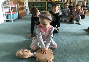 Nauka prawidłowego wykonywania RKO. Na pierwszym planie widoczna jest dziewczynka. W tle widoczne są dzieci. Ujęcie 3