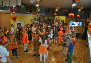 Dzieci i nauczyciele wspólnie bawią się na balu jesieni. Uczestnicy balu są poprzebierani w stroje związane z tematyką imprezy. Ujęcie 1