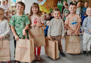 Dzieci, które otrzymały w konkursie nagrody pozują do wspólnego zdjęcia. W tle pozostałe dzieci z przedszkola. Ujęcie 1