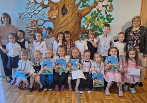 Dzieci i nauczycielki pozują do wspólnego zdjęcia z okazji "Pasowania na przedszkolaka" młodszych kolegów. Dzieci trzymają w rękach pamiątkowe dyplomy.