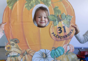 Dzień dyni w grupie 3. Dziecko pozuje do zdjęcia z makietą dyni.
