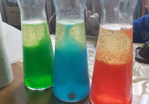 Zbliżenie na trzy flakony z płynami w kolorach: zielonym, niebieskim i czerwonym.