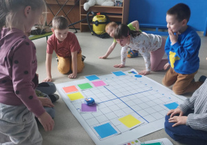 Dzieci siedzą dookoła planszy do kodowania i przyglądają sie zaprogramowanemu przez siebie robotowi.