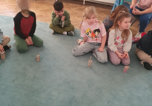 Dzieci siedzą na dywanie. Przed dziećmi stoją wykonane prace - kotki z tekturowych rolek po papierze toaletowym. Ujęcie 6