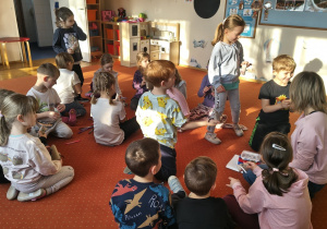 Grupa dzieci i nauczycielka siedzą na dywanie.