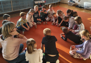 Dzieci i nauczycielka siedzą na dywanie. Przed dziećmi stoją wykonane prace - kotki z tekturowych rolek po papierze toaletowym. Ujęcie 2