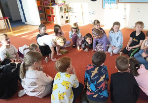 Dzieci i nauczycielka siedzą na dywanie. Przed dziećmi stoją wykonane prace - kotki z tekturowych rolek po papierze toaletowym. Ujęcie 3