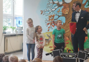 Iluzjonista w trakcie występu. Ujęcie 4. Artyście towarzyszy troje dzieci.