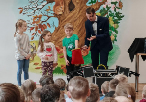 Iluzjonista w trakcie występu. Ujęcie 6. Artyście towarzyszy troje dzieci.